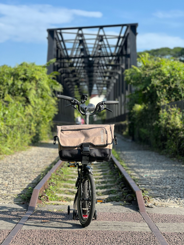 Brompton folding bike in front of an old truss bridge along the Rail Corridor in Singapore.