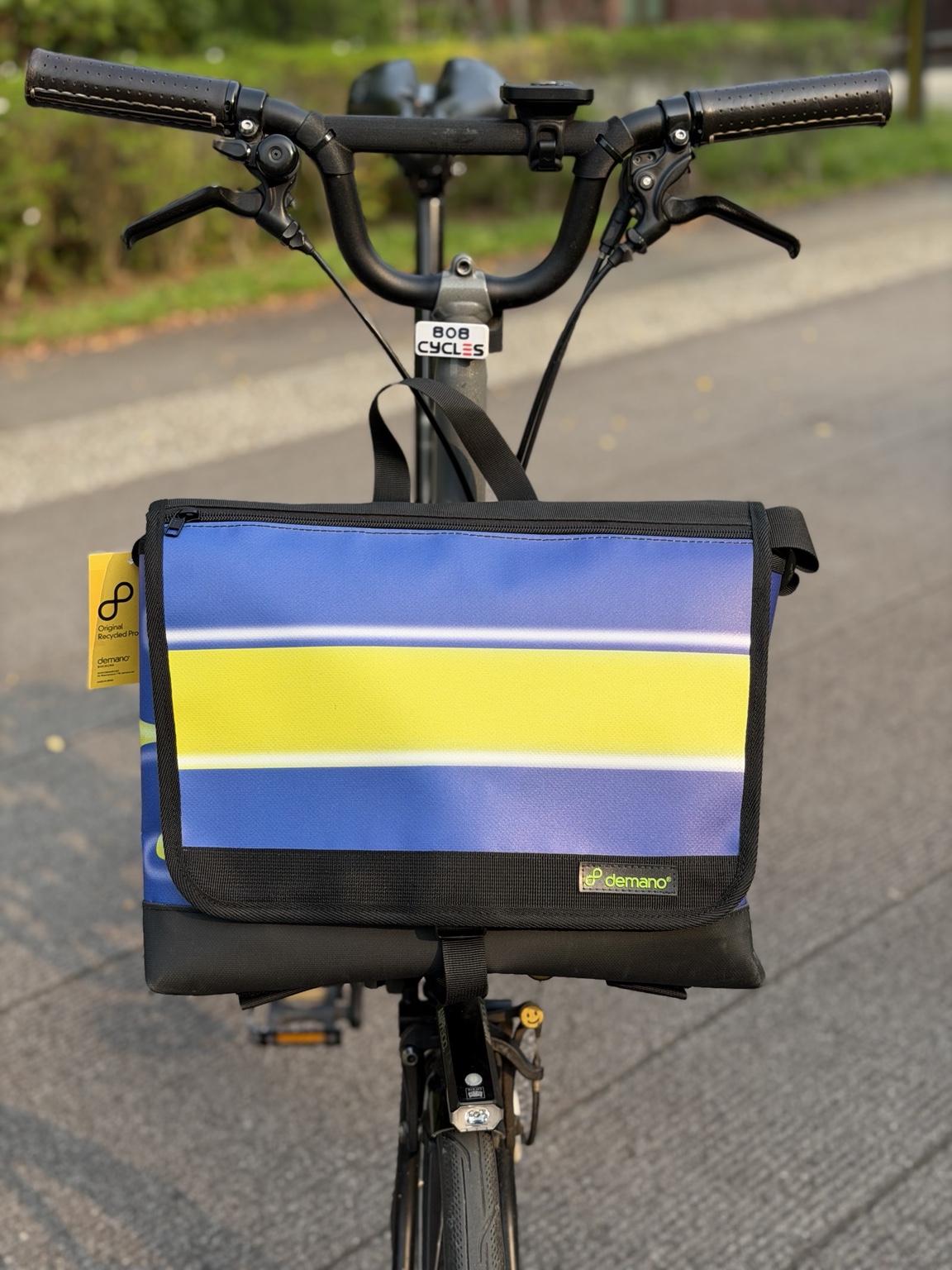 Front view of the actual Demano Arago 1711 on a Brompton, showing a broad yellow stripe with white outlines across blue-purple panels and black trim.