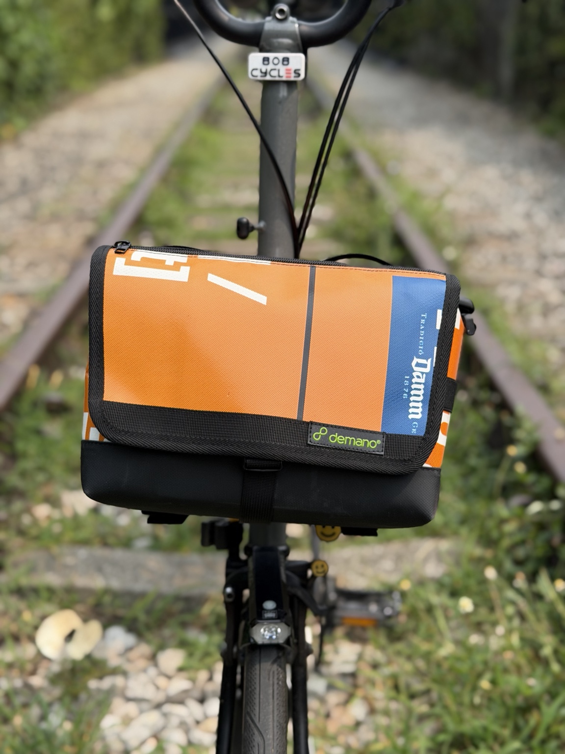 Front view of the actual orange-and-blue Demano Ribera 1703 bag mounted on a Brompton.