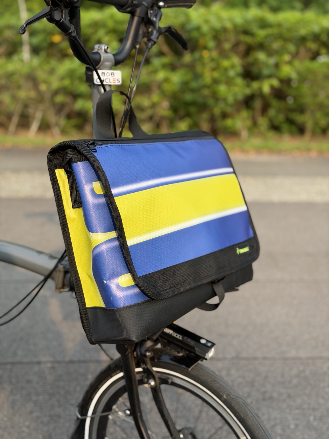 Left three-quarter view of Demano Arago 1711, showing the yellow band across the blue-purple flap and the left-side yellow and blue cropped banner shapes.