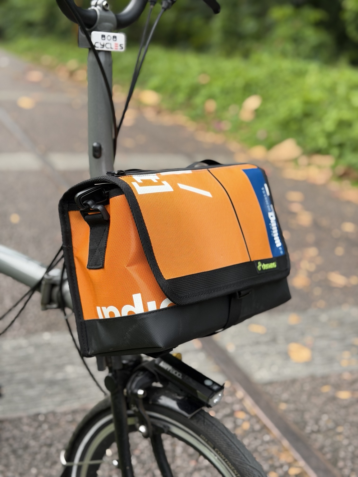 Left three-quarter view of Demano Ribera 1703 showing the orange panel, blue flap accent and black side hardware.