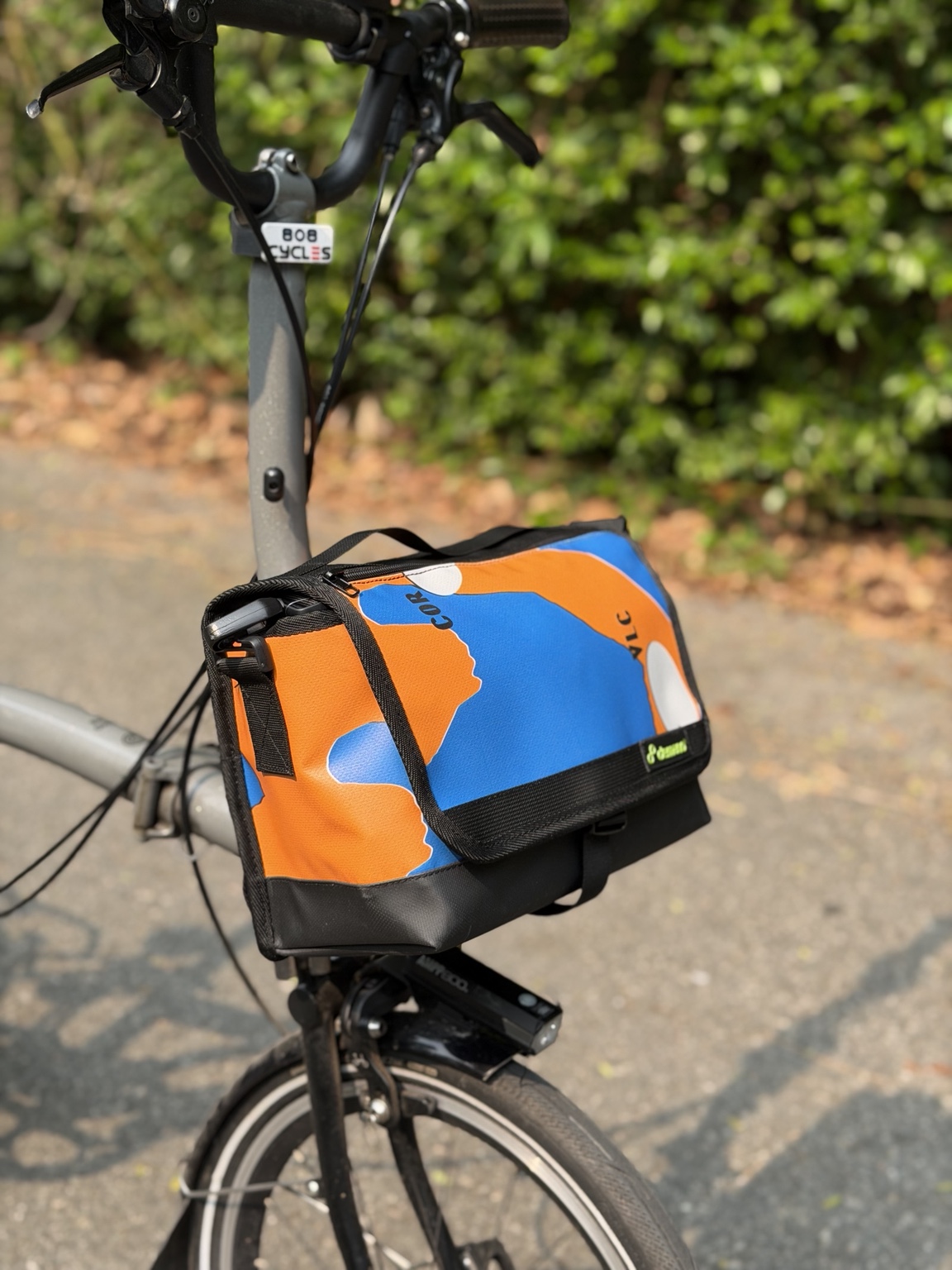 Left three-quarter view of Demano Ribera 1706 showing the blue-and-orange front graphic, orange side with blue shapes and black strap hardware.