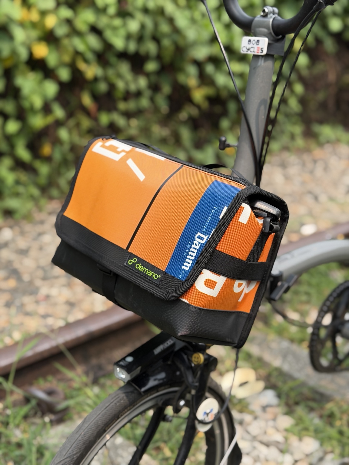 Right three-quarter view of Demano Ribera 1703 with orange banner canvas, blue flap stripe and black trim.