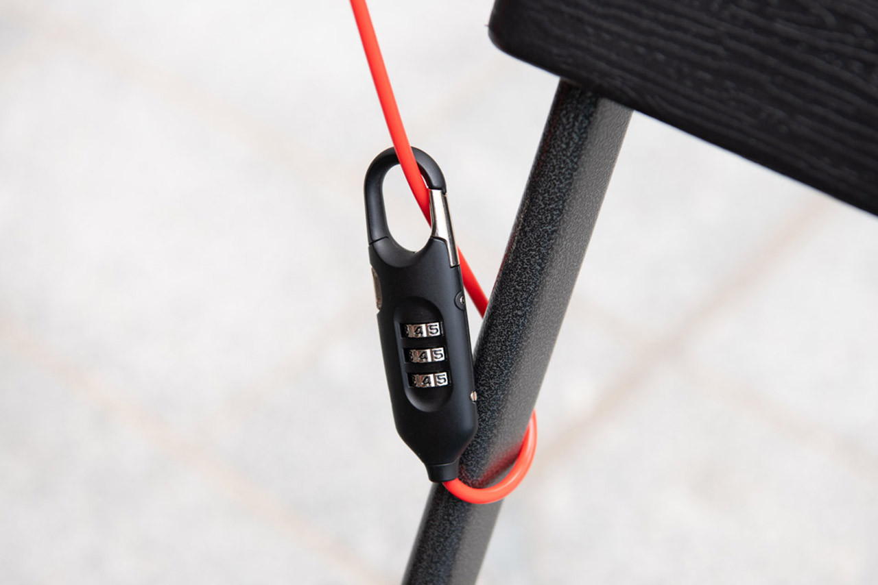 Black Brompton Cafe Lock with bright red cable looped around a chair leg, illustrating nearby short-stop use.