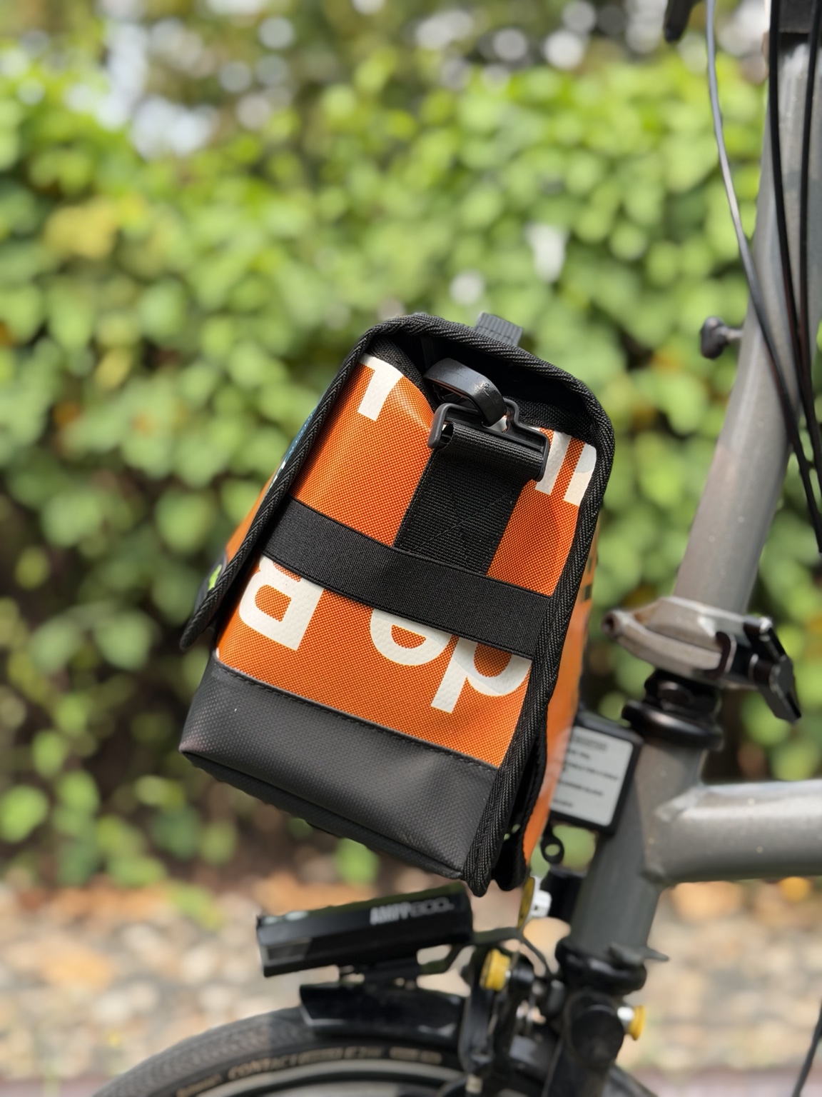 Right-side profile of Demano Ribera 1703 showing black strap hardware and horizontal webbing over orange banner canvas.