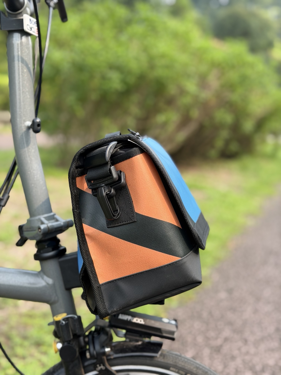Left-side profile of Demano Ribera 1705 with orange banner canvas, a broad dark diagonal print, black hardware and reinforced black base.