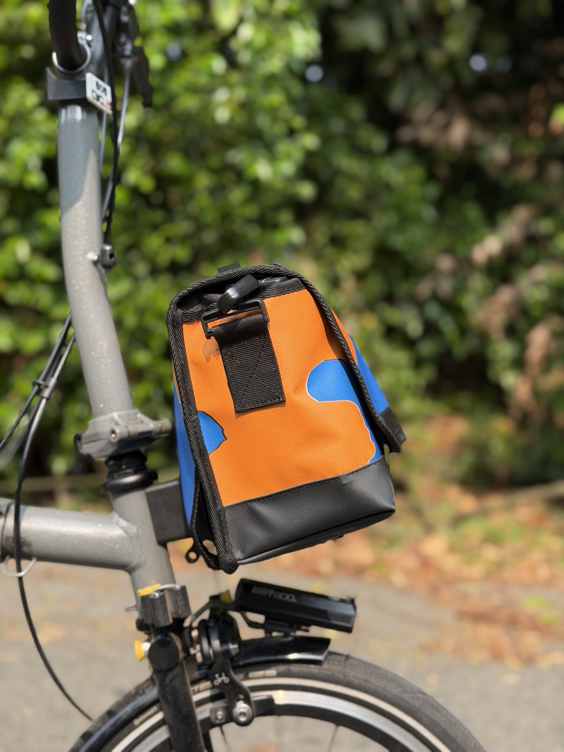 Left-side profile of Demano Ribera 1706 showing orange banner canvas with blue shapes, black hardware and a reinforced black base.