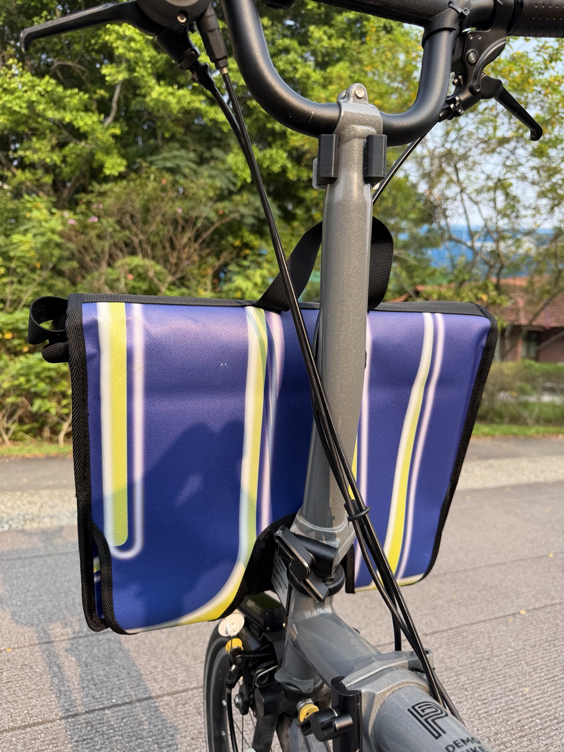 Original rear view of Demano Arago 1711 mounted on a Brompton, showing blue-purple panels and curved yellow-white banner lines behind the bicycle stem.