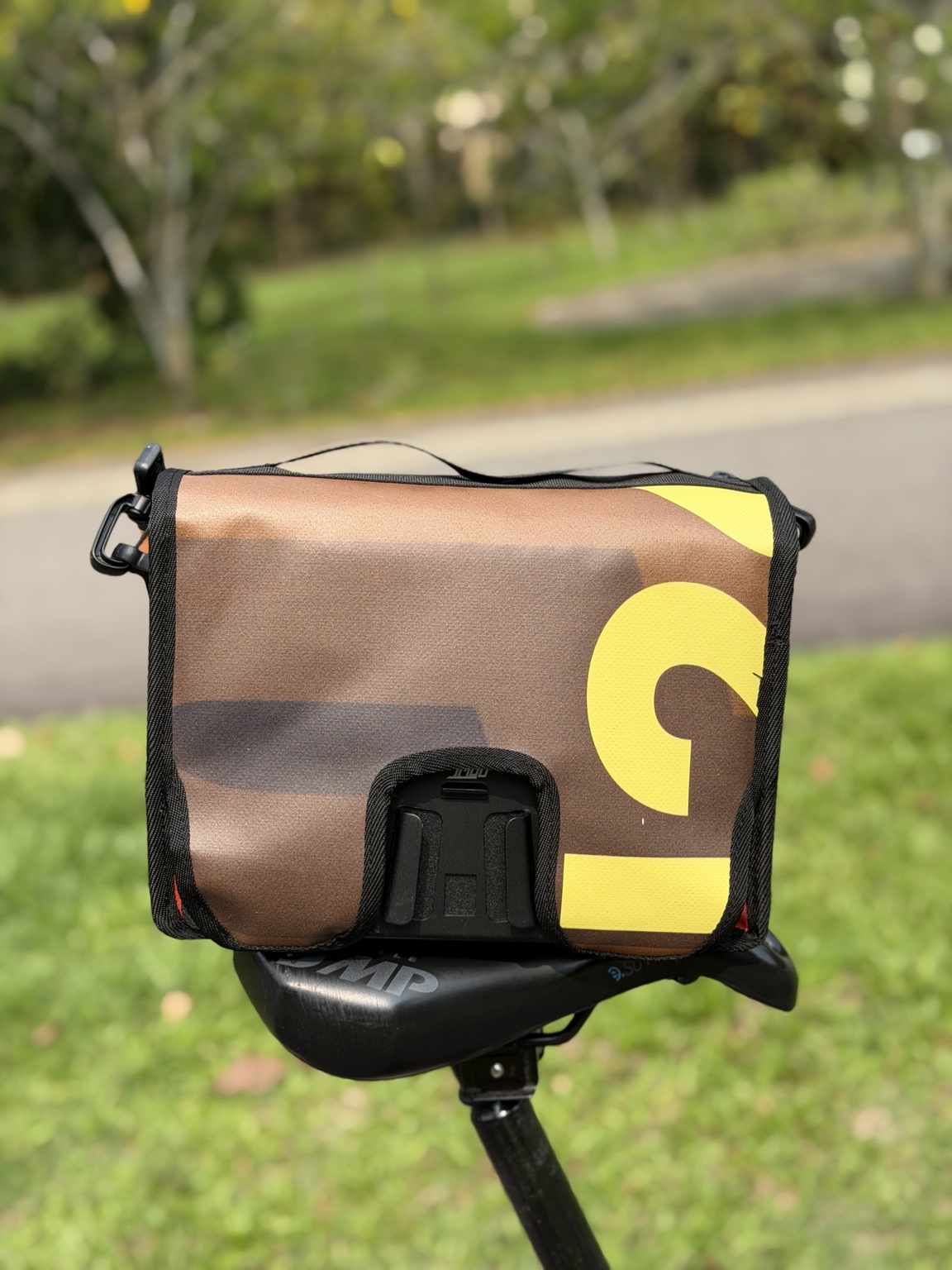 Rear view of Demano Ribera 1710 resting on a bicycle saddle, showing cropped yellow banner lettering on brown-burgundy panels and the actual rear mounting interface.