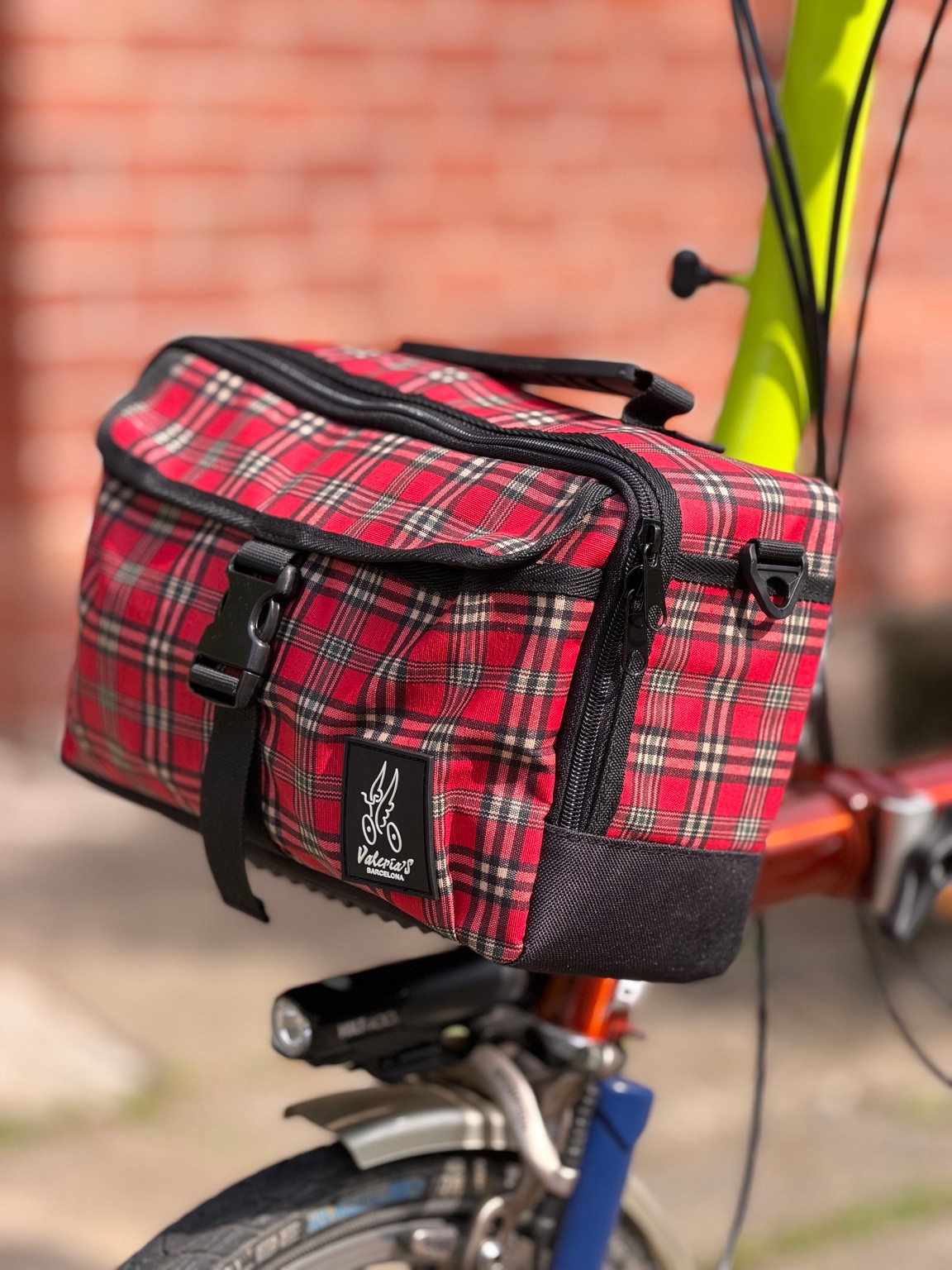 Three-quarter view of Valeria’s Cris Mini #04 showing red tartan panels, black trim, zipped top and shoulder-strap attachment
