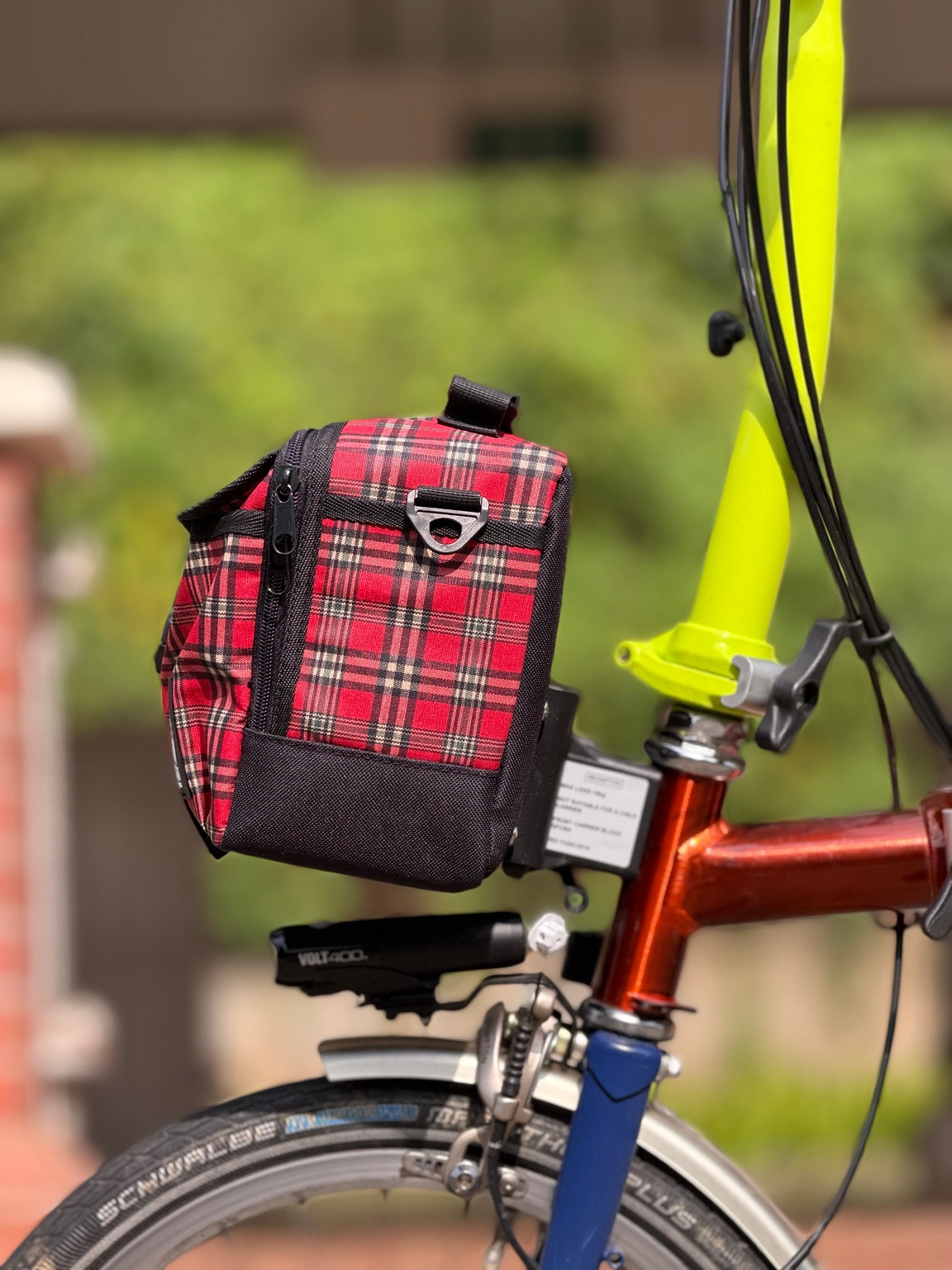 Side view of Valeria’s Cris Mini #04 red tartan bag showing the black lower panel, strap attachment and Brompton front mounting position