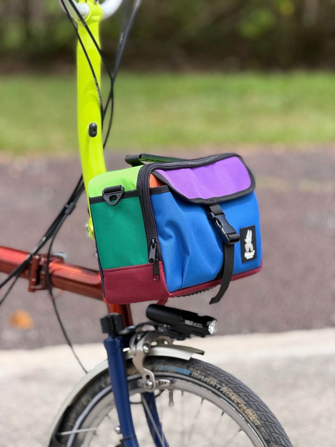 Valeria’s Cris Mini #01 multicolour 5L bag on a Brompton, three-quarter front view showing flap buckle and zip