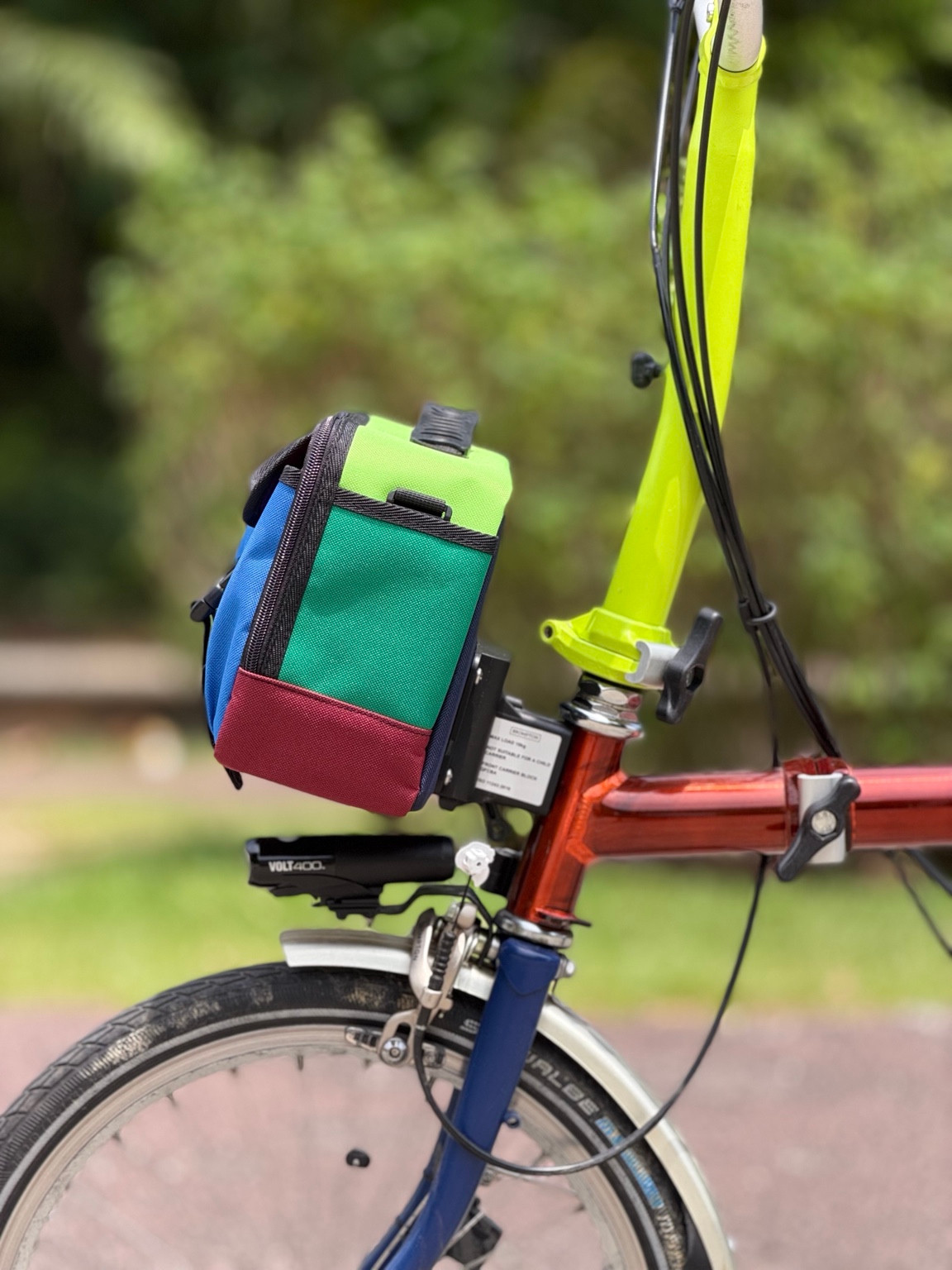 Side view of Valeria’s Cris Mini #01 bag mounted on a Brompton, showing green panel and burgundy base